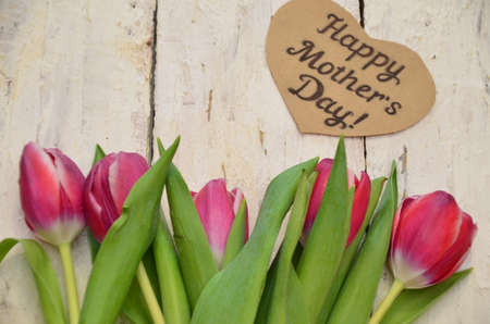 Tulips and a heart with the inscription happy mother day of Mom and gifts on a white wooden background.の写真素材