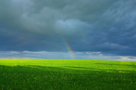end of rainbow above the green field on a background a dark cloudの写真素材