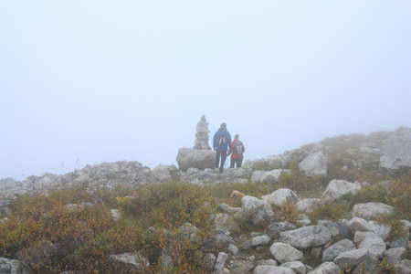 two hikers near the path pointer on a high-mountainous trail in a fogの写真素材