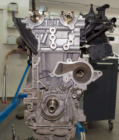 Front view of an automobile internal combustion engine with cast-iron exhaust and plastic intake manifolds without a valve cover, which is installed on a stand for engine repair