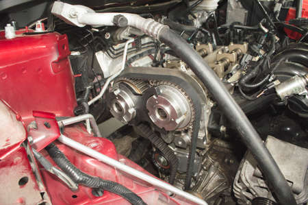Using a stop to lock the camshafts when replacing the timing belt on a red car in a car repair shopの写真素材