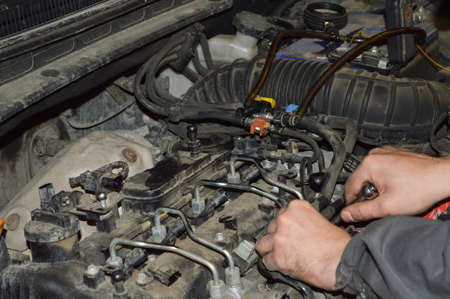 A car mechanic unscrews the fuel ramp on a diesel internal combustion engine