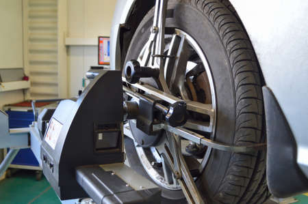 Camber-convergence adjustment stand sensor mounted on the front left wheel of a gray car in a car...