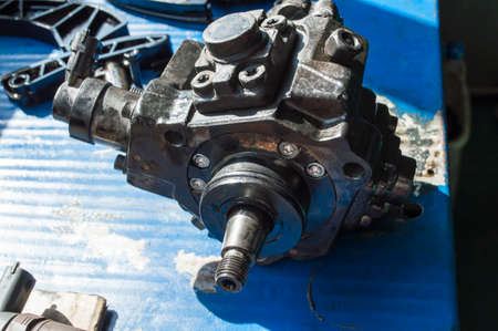 Top view of an old high-pressure fuel pump from a diesel car engine that lies on a blue work table...