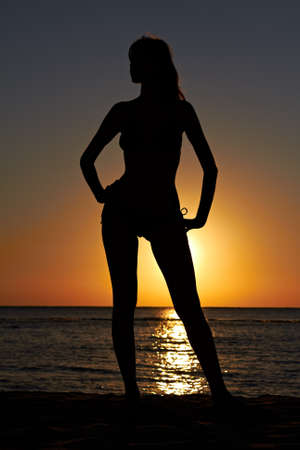 Silhouette of woman posing on sea coast at sunriseの写真素材