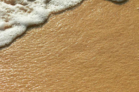 Wet coastline sand under under thin layer of water