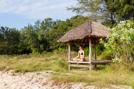 Young woman doing yoga lotus meditation in pavilion near oceanの写真素材
