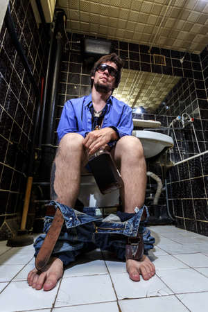 Drunk Man in a toilet with bottle of whiskey, Color image, extrime wide angleの写真素材