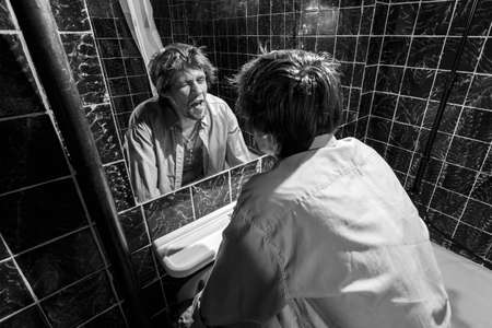 Drunk Man looks at himself in the mirror in a bathroom  grayscale imageの写真素材