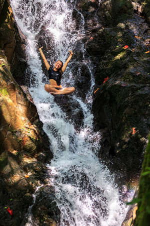 Carefree Woman enjoying in falling water with arms raisedの写真素材