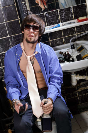 Drunk Man sits in a toilet with a bottle of whiskey Color imageの写真素材