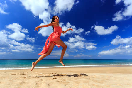 Happy girl in red dress jumping and running on beachの写真素材