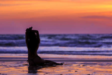 Silhouette young woman sitting on the beach at sunsetの写真素材