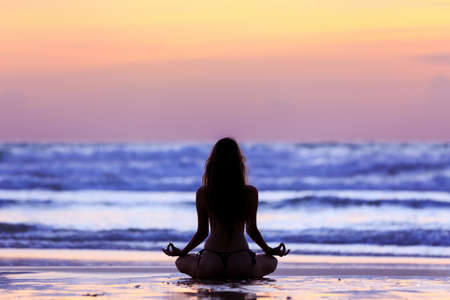 Silhouette young woman practicing lotus yoga on the beach at sunsetの写真素材
