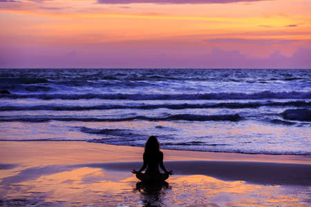 Silhouette young woman practicing lotus yoga on the beach at sunsetの写真素材