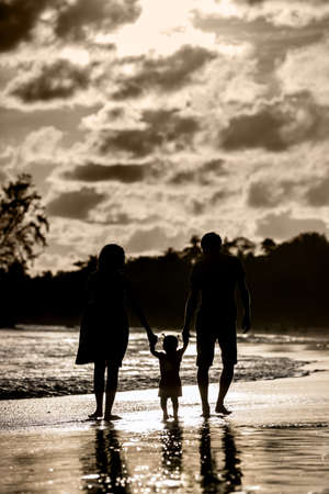 Silhouette of a family walking on the beach at sunsetの写真素材