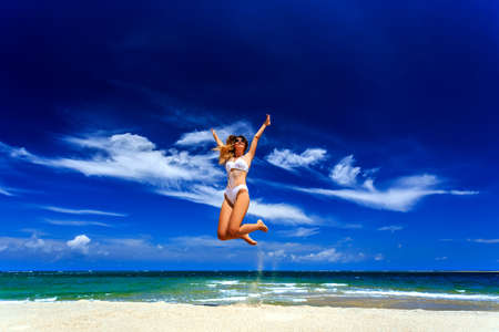 Happy girl in white bikini jumping at tropical beachの写真素材