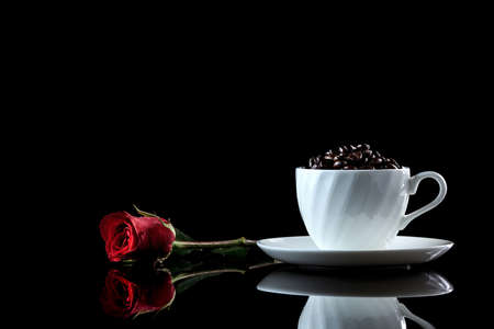 Cup with coffee beans and rose on a black reflective background. Studio shotの写真素材