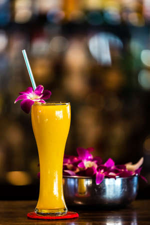Yellow cocktail with orchid flower in the bar on the blurred background. Verticalの写真素材