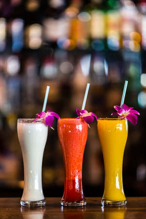 Vertical  composition with 3 yellow, white, red cocktails and orchid flowers on the blurred backgroundの写真素材