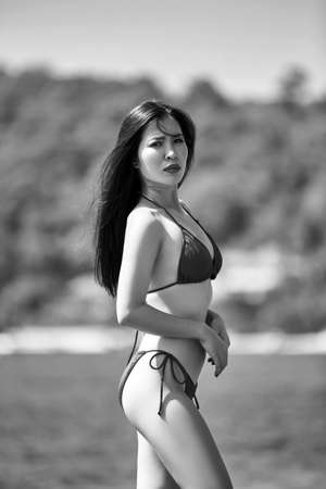Beautiful asian woman posing on a beach with rocks in a blue bikini, grayscale imageの写真素材