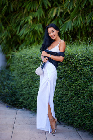 Outdoor full-length fashion portrait of young elegant woman holding classic handbag