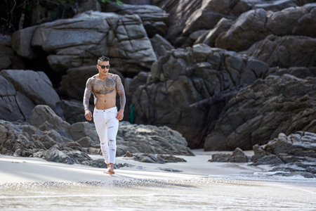Athletic shirtless tattooed guy walking at the tropical beachの写真素材