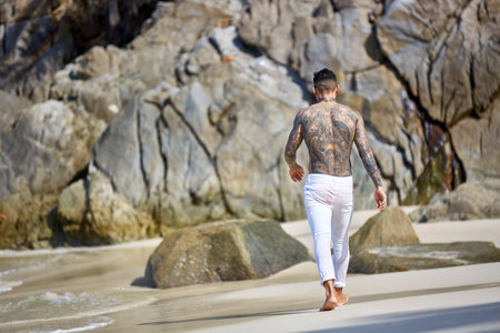 Athletic shirtless tattooed guy walking at the tropical beachの写真素材