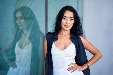 Outdoor close-up fashion portrait of young elegant woman holding classic handbag posing near to...