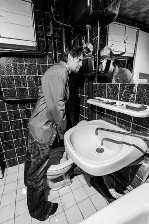 Drunk Man is standing in a toilet with a bottle of whiskeyの写真素材