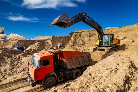 Yellow excavator working with sand at construction site in sunny dayの写真素材
