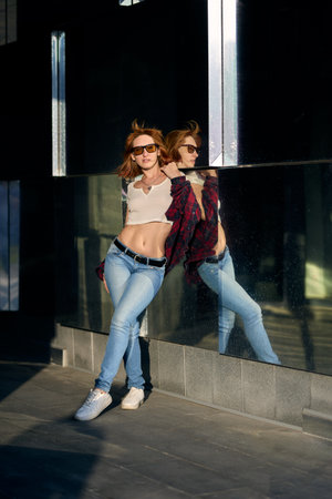 A fashionable redhead woman enjoying an autumn evening in the city. She's wearing a trendy red jacket, a white t-shirt, and denim jeans, making a bold fashion statementの写真素材