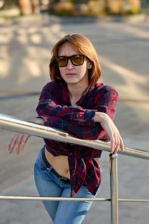 A fashionable redhead woman enjoying an autumn evening in the city. She's wearing a trendy red jacket, a white t-shirt, and denim jeans, making a bold fashion statementの写真素材