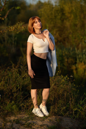 A redhead woman in a white top poses gracefully in the warm glow of an autumn sunsetの写真素材