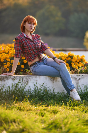A fashionable redhead woman enjoying an autumn evening in the city. She's wearing a trendy red shirt and denim jeans, making a bold fashion statementの写真素材