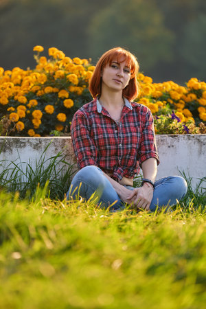 A fashionable redhead woman enjoying an autumn evening in the city. She's wearing a trendy red shirt and denim jeans, making a bold fashion statementの写真素材