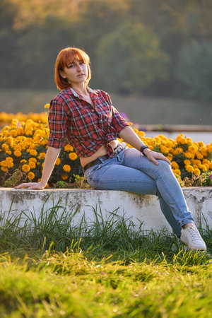 A fashionable redhead woman enjoying an autumn evening in the city. She's wearing a trendy red shirt and denim jeans, making a bold fashion statementの写真素材