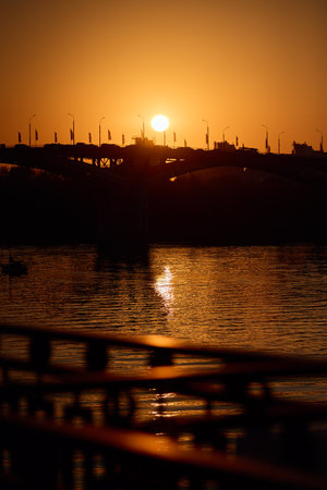Golden Bridge Sunset: Radiant sun, tranquil water, and silhouetted bridgeの写真素材