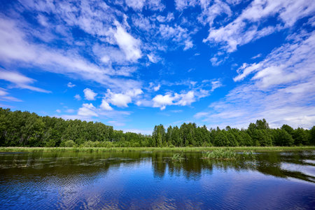 Beautiful summer landscape of river at sunny day with sky and clouds reflection in the waterの写真素材