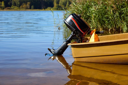 A serene lake view featuring a moored boat with an outboard motor and lush greenery. Perfect for nature and outdoor adventure themesの写真素材