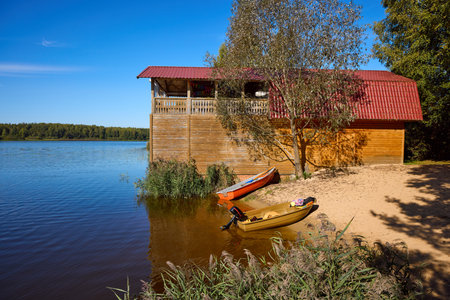 Wooden house by the lake with canoes on sandy shore, under clear blue sky - perfect for leisure or vacation themesの写真素材