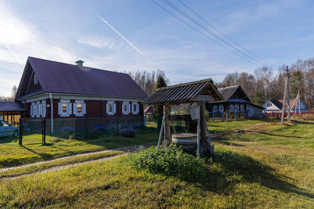 A serene morning scene featuring an old wooden well in a rural village, surrounded by traditional houses and lush greenery under a clear blue skyの写真素材