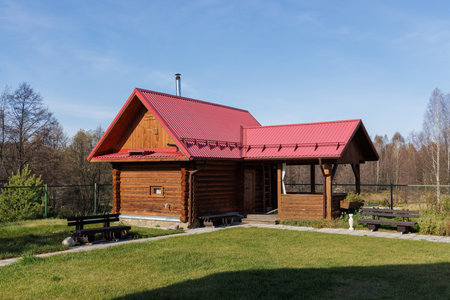 A cozy wooden cabin with a red roof set in vibrant greenery, showcasing tranquility and natural beautyの写真素材