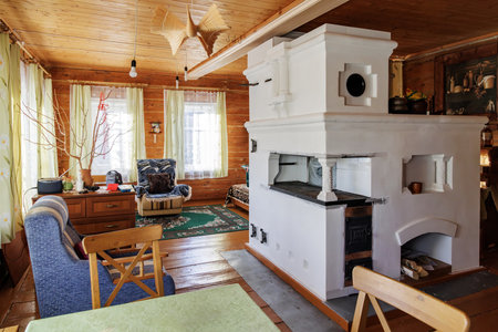 A traditional Russian stove in a cozy wooden house interior, featuring wooden walls, a ceiling, and a mix of modern and rustic furnitureの写真素材