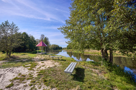 A peaceful scene of a red-roofed gazebo surrounded by lush greenery under a blue skyの写真素材