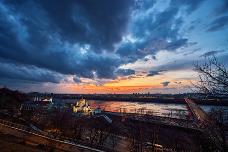 A striking winter sunset over the Annunciation Monastery and Kanavinsky Bridge in Nizhny Novgorod, Russia. The golden domes, illuminated clouds, and frozen river create a breathtaking sceneの写真素材