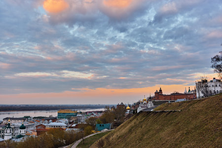 A picturesque sunset side view of the Nizhny Novgorod Kremlin, with the domes of Kazan Church glowing softly against a colorful sky and the Volga River in the backgroundの写真素材
