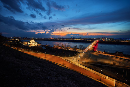 A mesmerizing sunset over Strelka in Nizhny Novgorod, featuring Kanavinsky Bridge and the illuminated Alexander Nevsky Cathedral. The frozen river and glowing city lights create a stunning winter viewの写真素材