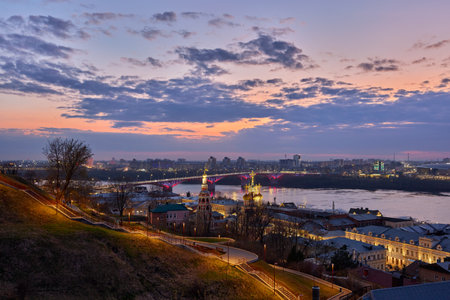 A magical twilight view of Strelka in Nizhny Novgorod, showcasing the lit-up Kanavinsky Bridge and Rozhdestvenskaya Church reflecting on the Oka Riverの写真素材