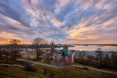 A serene sunset over Strelka in Nizhny Novgorod, featuring the Oka River, Rozhdestvenskaya Church, and Alexander Nevsky Cathedral under a colorful sky with soft reflectionsの写真素材